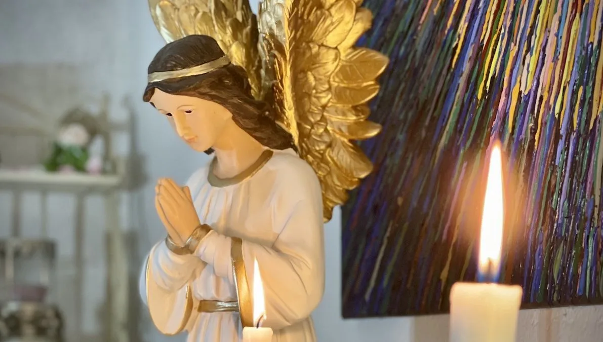 Figura de ángel en oración junto a una vela, sanación con ángeles